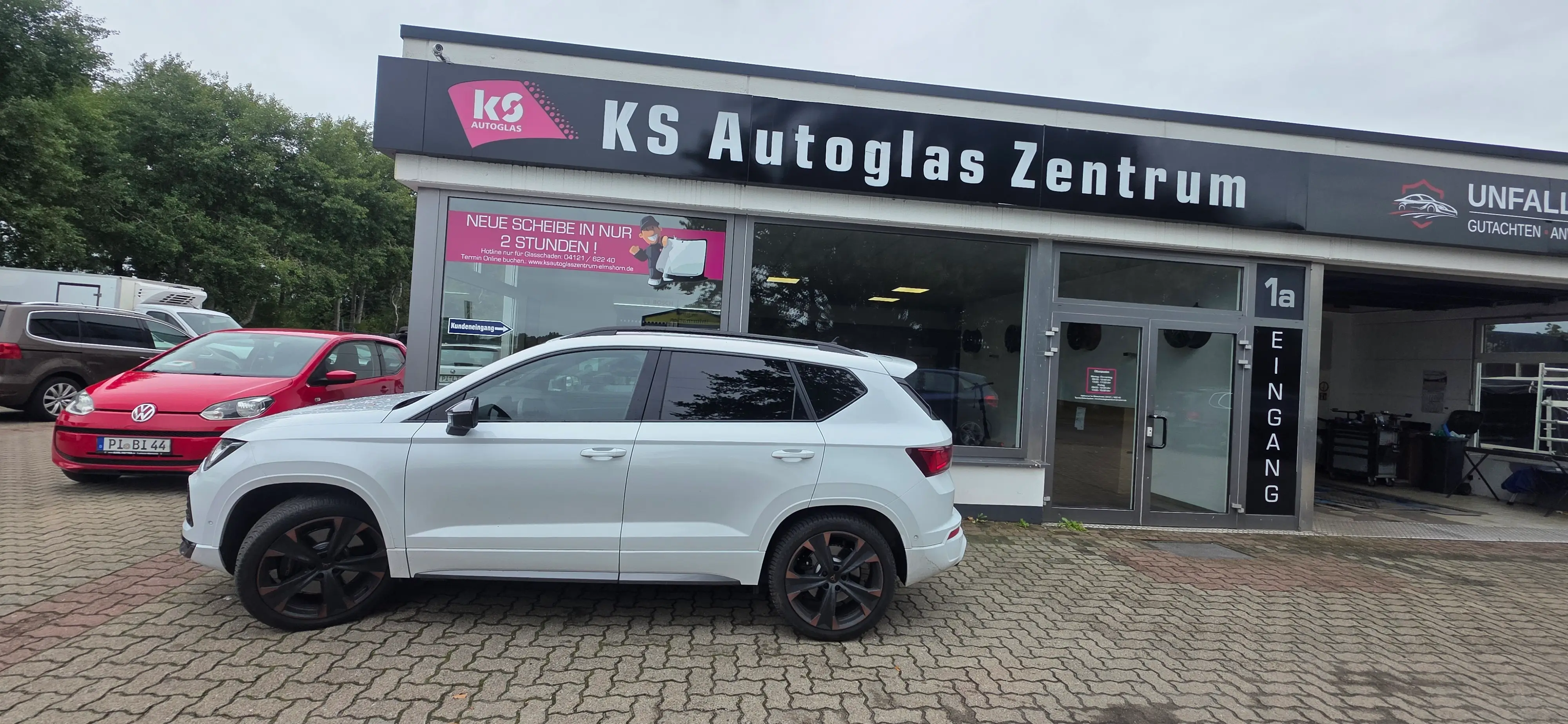 Ein weißer SUV mit getönten Scheiben steht vor dem KS Autoglas Zentrum Elmshorn, im Hintergrund sind weitere Fahrzeuge und das Gebäude sichtbar.